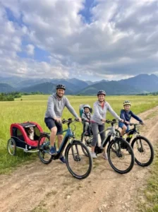 Rodzina na rowerach z przyczepką dla dziecka na polnej drodze na tle gór