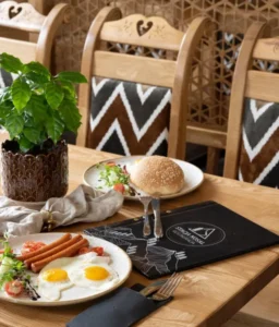 Śniadanie z jajkiem sadzonym, kiełbaskami i bułką podane na stole obok menu z logo Stacja Nosal