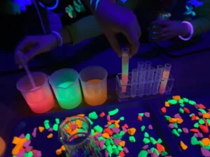 Ciemne pomieszczenie z fluorescencyjnymi materiałami i rękami dzieci pracujących nad eksperymentami