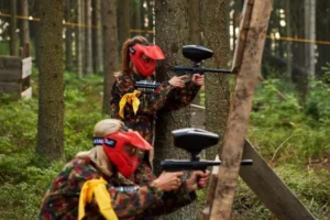 Dwie osoby strzelające z markerów paintballowych z ukrycia między drzewami w lesie