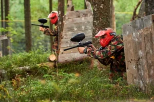 Dwie osoby z markerami paintballowymi między drzewami w lesie