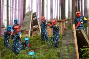 Grupa osób w kaskach i kombinezonach trzymająca sprzęt do paintballa w lesie