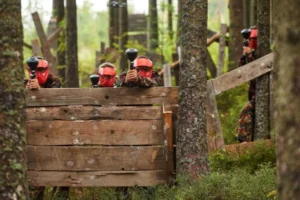 Osoby ukrywające się za drewnianą zasłoną z desek na terenie paintballowym