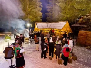 Grupa ludzi nocą przy oświetlonym szałasie góralskim w towarzystwie górali